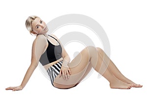 A teenage girl sits in a sports swimsuit. A thoughtful blonde with freckles on her face in a black top and striped panties.