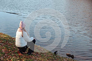 Teenage girl sitting from behind wearing casual fall clothes in an autumn park with lake outdoors