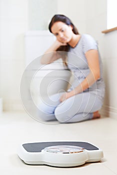 Teenage Girl Sitting On Floor Looking At Bathroom Scales