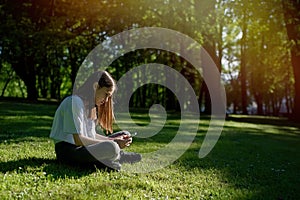 Teenage girl sitting on the grass and using a smartphone