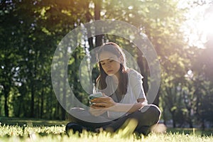 Teenage girl sitting on the grass and using a smartphone