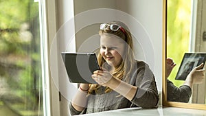 Teenage girl sitting near the window with a tablet in hand.