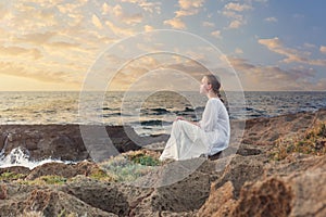 Teenage girl sitting on rocks near blue sea