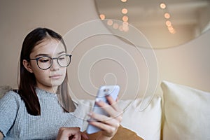 Teenage girl sitting on sofa at home and using mobile phone