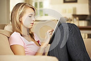 Teenage Girl Sitting On Sofa At Home Using Tablet Computer