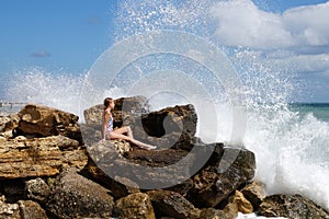 Teenage girl sitting on a stone on the seashore under the splashing waves