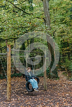 A teenage girl sitting on a swing on the park. Pensive sad child. Thoughtful Sad Teenager Girl Sitting On Playground