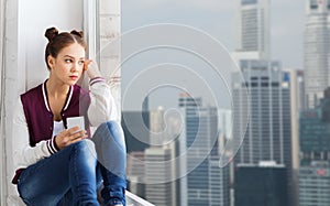 Teenage girl sitting on windowsill with smartphone