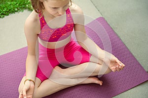 Teenage girl sitting in yoga pose and meditating on yoga mat in sport uniform