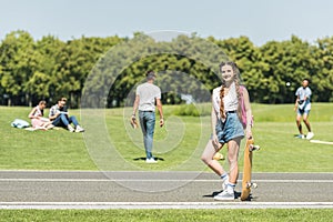 teenage girl with skateboard smiling at camera while friends spending time behind