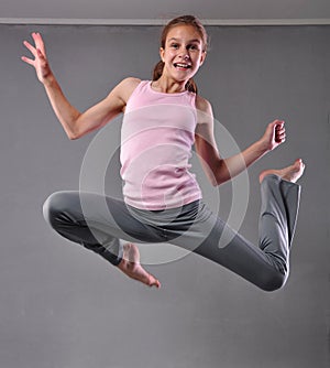 Teenage girl skipping and dancing in studio. Child exercising with jumping on grey background.