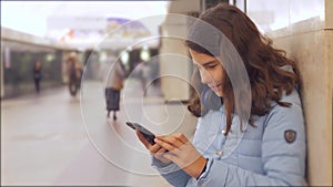 Teenage girl with smartphone and headphones waiting subway lot of people crowd underground crossing. Metro lifestyle