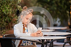 teenage girl with a smartphone in her hands sits at a table in summer cafe