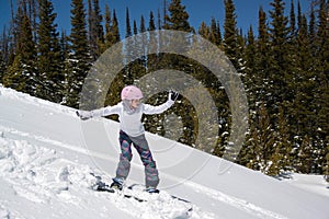 Teenage girl snowboarding down snowy hill in the mountains