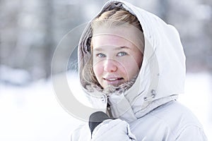 Teenage girl in a snowy winter park. Smiling blonde woman in a white jacket with fur. Close-up