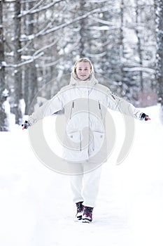 Teenage girl in a snowy winter park. Smiling blonde woman in a white jacket with fur. Full height. Vertical