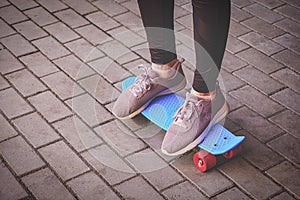 Teenage Girl In Spurt Shoes is standing on small pennyboard skateboard on footpath