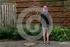 Teenage girl standing alone with her back to the viewer against the background of an old wall