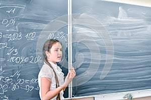 Teenage girl standing and answering at the blackboard in math class. Education, back to school concept, copy space.