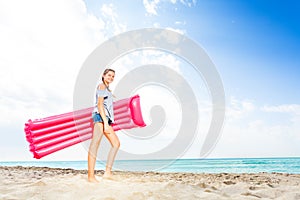 Teenage girl standing with matrass on sandy beach