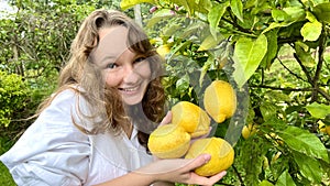 a teenage girl is standing near a lemon tree she is holding a lemon in her hands she is sniffing it she is going to make