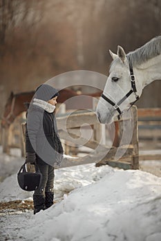 Teenage girl standing near white horse in a paddock