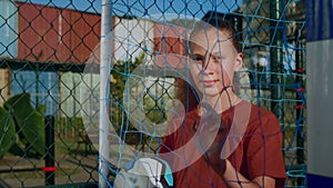 Teenage girl stands with ball on football field and looks into distance through net closeup