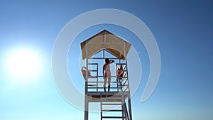 Teenage girl stands on lifeguard tower on beach against cloudless sky.
