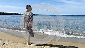 Teenage girl in a striped dress on the seashore on a sunny day, rear view