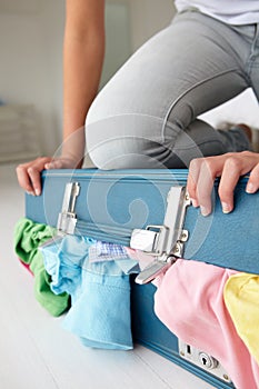 Teenage girl struggling to shut suitcase