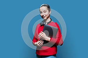 Teenage girl student in headphones with laptop in hands on blue background