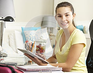 Teenage Girl Studying At Desk In Bedroom Using Digital Tablet