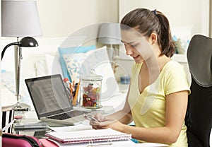 Teenage Girl Studying At Desk In Bedroom Using Mobile Phone
