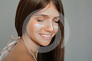 Teenage girl with sun protection cream on her face against grey background, closeup