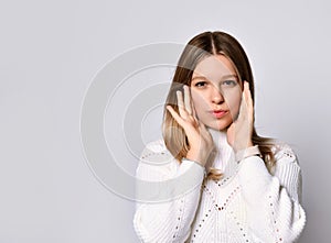 Teenage girl in sweater, smart watch and bracelet. She is looking at you, touching her face, posing isolated on white. Close up