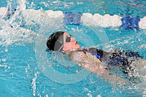 Teenage girl doing backstroke in school swim meet competition photo