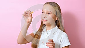 Teenage girl takes omega 3 capsules on a colored background close-up