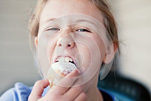 Teenage girl taking a big bite out of a sugary pastry.