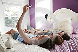 Teenage girl taking a selfie with two friends lying on a bed