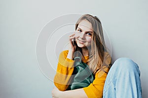 Teenage girl talking on a cellphone and smiles looking at camera. Beautiful girl in yellow sweater and blue jeans holding mobile p