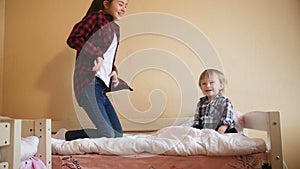 Teenage girl with toddler boy laughing and jumping on bed