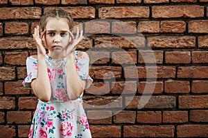 Teenage girl touches fingers near temples, against a brick wall, headache