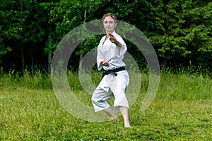 Teenage girl training karate kata outdoors, performs soto uke or outside block in kakutsu dachi stand photo