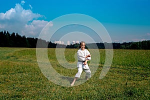 Teenage girl training karate kata outdoors, prepares to perform downward block gedan barai in zenkutsu dachi stance