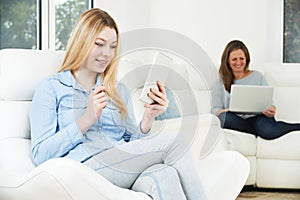 Teenage Girl Uses Digital Tablet Whilst Mother Works On Laptop