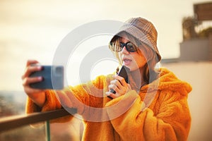 Teenage girl uses smartphone, standing next to glass railing balcony