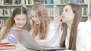 Teenage girl using her laptop while studying at the library with friends