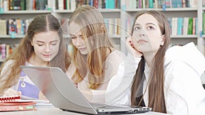 Teenage girl using her laptop while studying at the library with friends