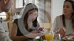 Teenage girl using mobile phone during breakfast at the table.