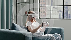 Teenage girl with VR controllers moves hands sitting on sofa